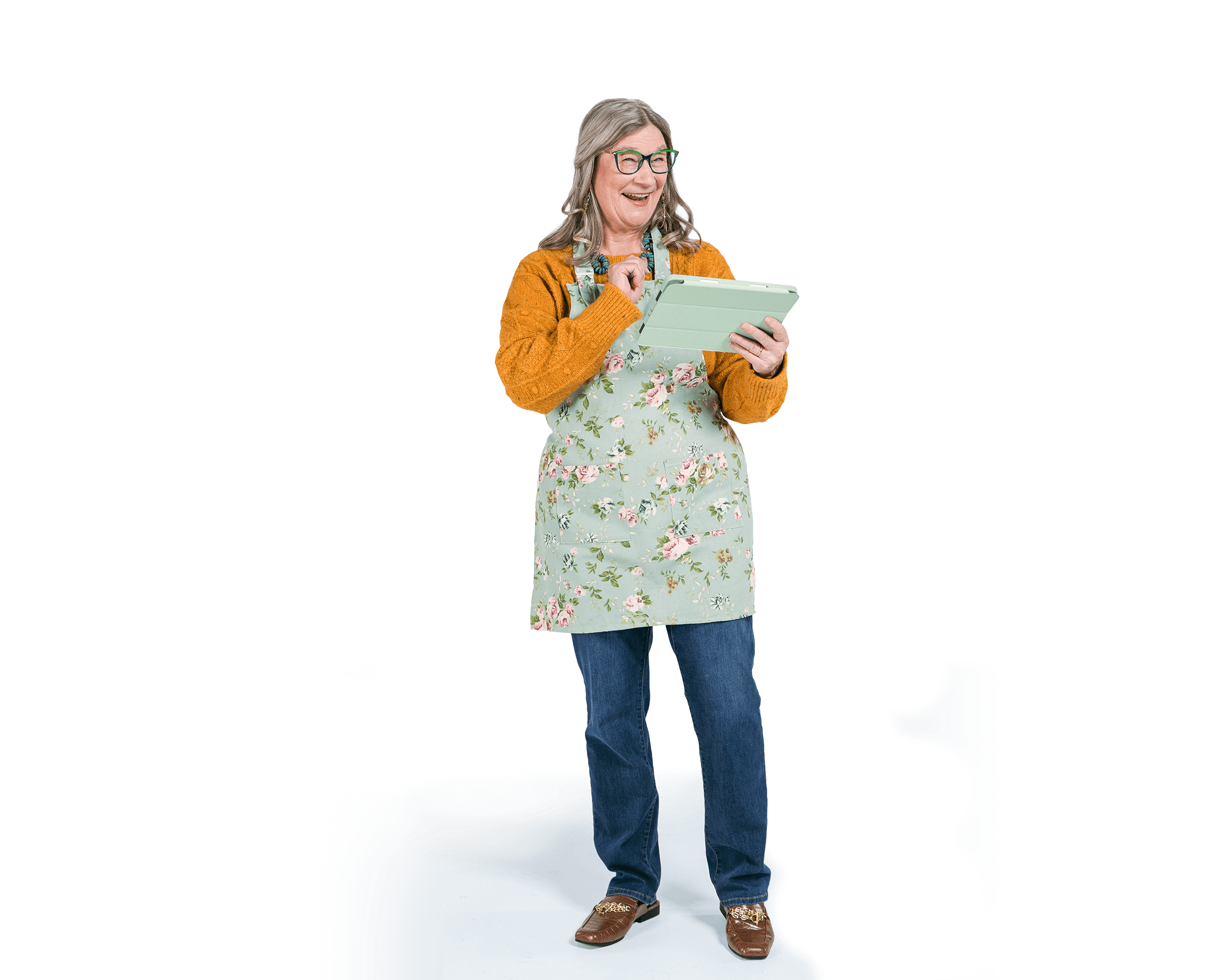 Woman with gray hair and glasses wearing an apron smiling and using a tablet
