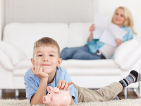 Child laying on the floor smiling with his piggy bank.