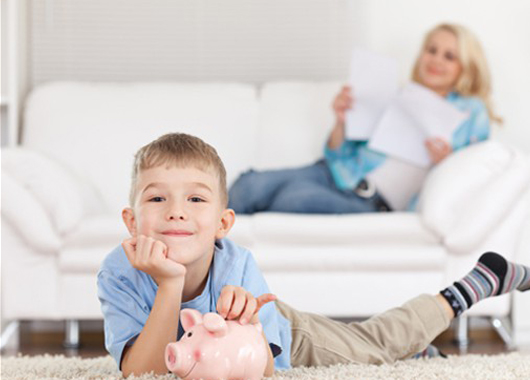 Child laying on the floor smiling with his piggy bank.