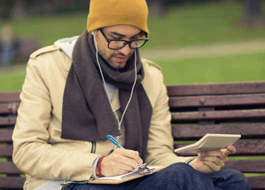 Young man sitting on a park bench reviewing his finances.