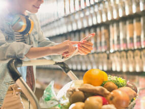 Woman shopping for groceries holding cell phone.