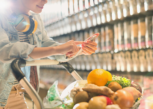 Woman shopping for groceries holding cell phone.