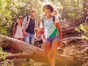 Group Of Friends Jumping Over Tree Trunk On Countryside Walk