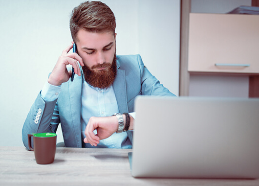 Businessman looking at watch while working on laptop.