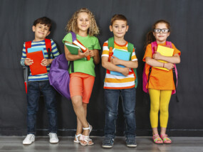 Four children holding their books and backpacks ready for school to start.