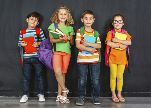 Four children holding their books and backpacks ready for school to start.