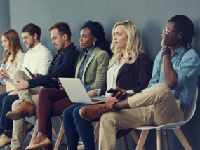 Group of people sitting in a line of chairs waiting for a job interview.