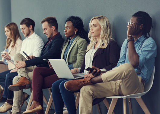 Group of people sitting in a line of chairs waiting for a job interview.