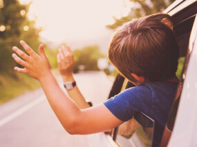 Kids hanging heads and hands out of a car window.