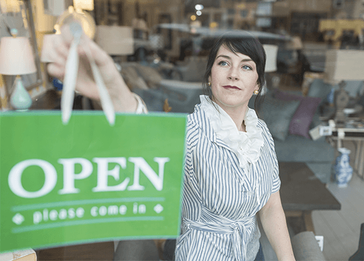 small business owner placing open sign in store window|New business owner checking her online banking on her tablet.