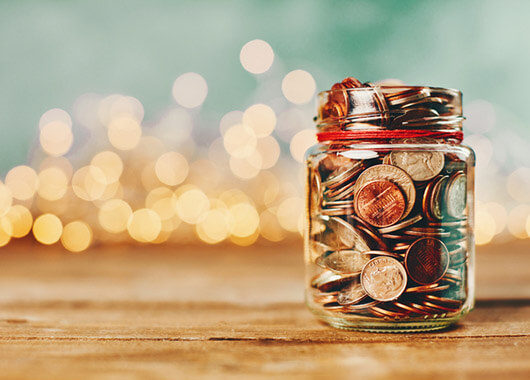 Jar of change with Christmas lights in the distance behind it.