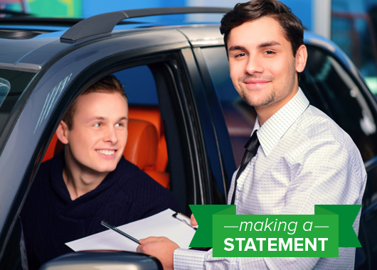Car salesman handing paper work to a young man sitting in car.