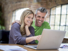 Happy online couple working on a laptop computer to refinance mortgage