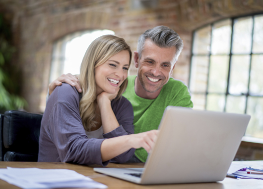 Happy online couple working on a laptop computer to refinance mortgage