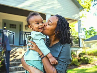 Mom holding a toddler in the front lawn of their house