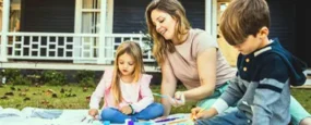 Mom and kids painting a picture while sitting on their lawn