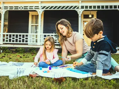 Mom and kids painting a picture while sitting on their lawn