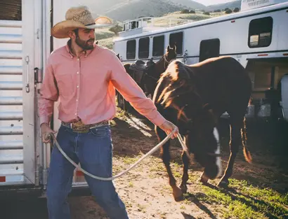 Cowboy walking his horse to a trailer