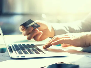 Man typing on computer while holding a credit card