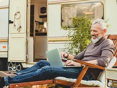 Elderly man sitting outside his RV on his computer
