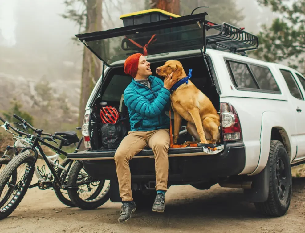 man petting dog while sitting on the back of his car