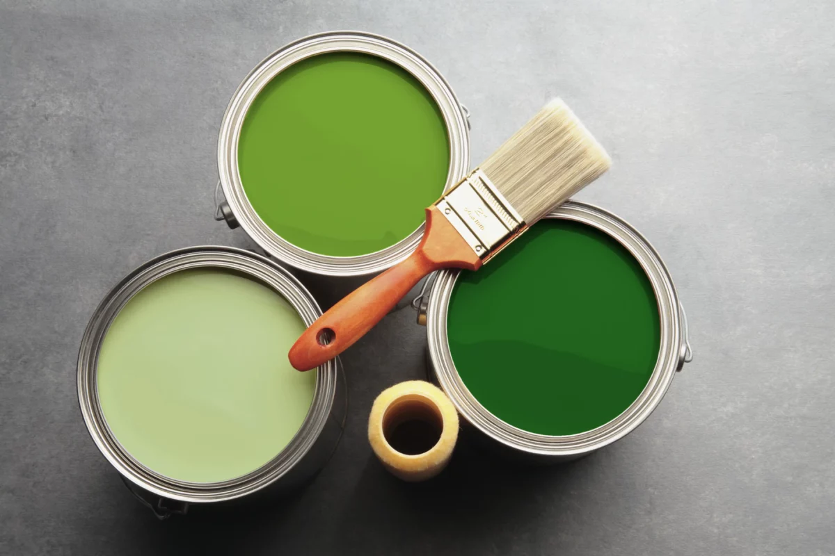 paint brush laying on cans of green paint