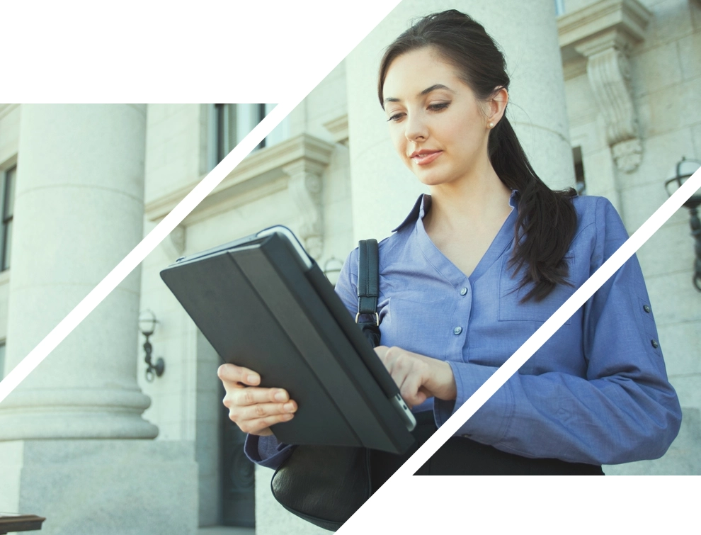 business casual woman standing outside a building looking down at her tablet
