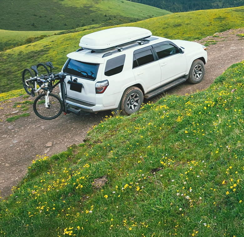 white suv with bike on the back going up side of grassy hill