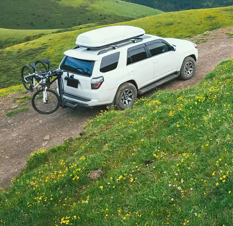 white suv with bike on the back going up side of grassy hill