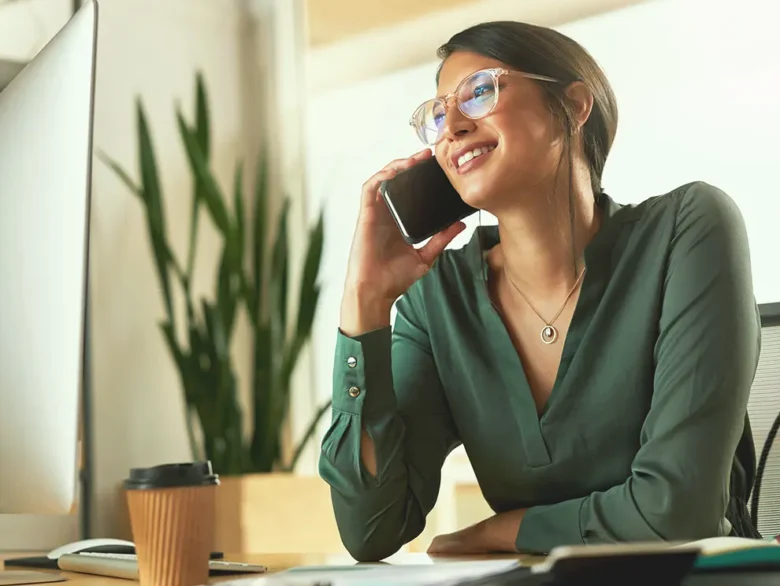 Person on phone at desk with computer and coffee.