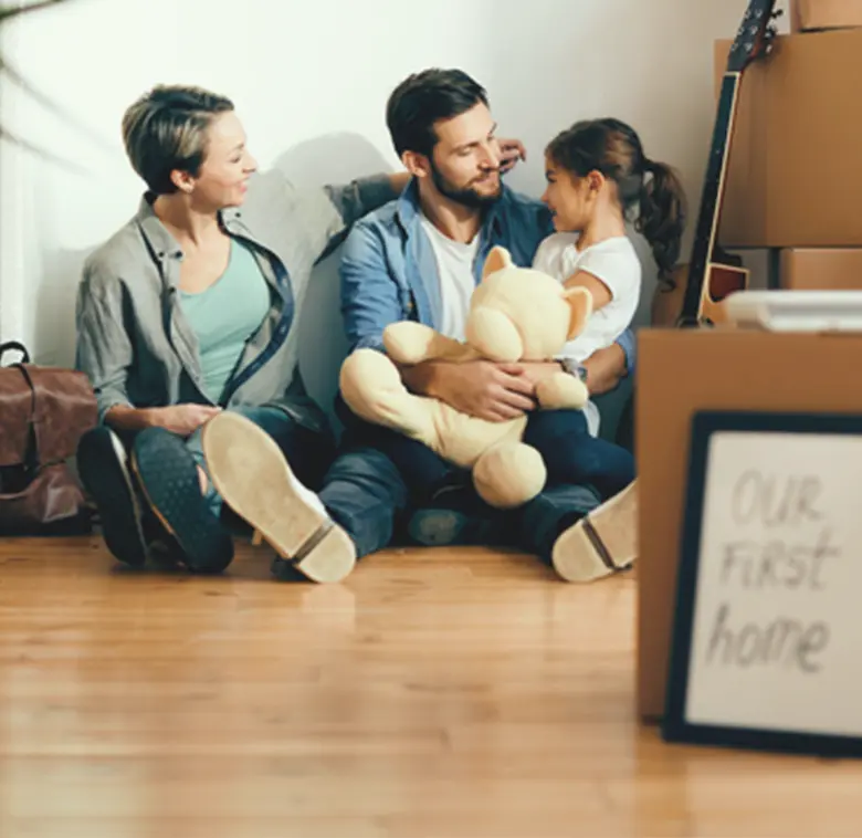 Family in new home with moving boxes and 'Our First Home' sign.