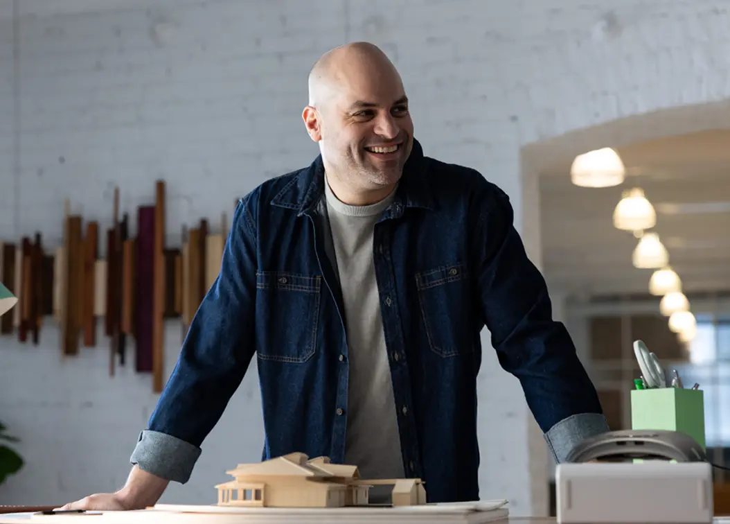 Male business owner standing confidently in his workspace, smiling and dressed in casual business attire.