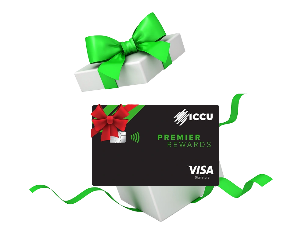 ICCU Premier Rewards Visa credit card with a red bow, placed in front of a white gift box wrapped with a green ribbon.