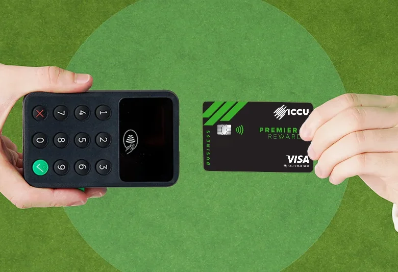 Hand holding ICCU Premier Rewards Visa Credit Card near a card reader for contactless payment.